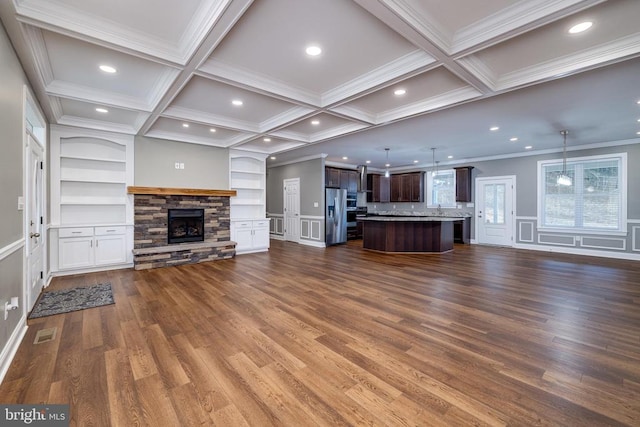 unfurnished living room with beam ceiling, dark wood-type flooring, coffered ceiling, a stone fireplace, and ornamental molding