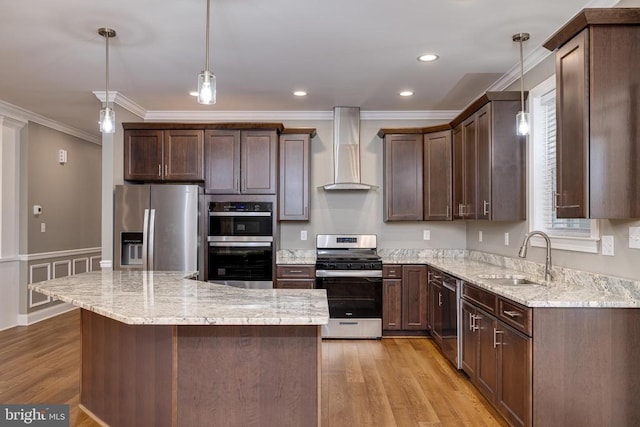 kitchen featuring appliances with stainless steel finishes, wall chimney exhaust hood, sink, light hardwood / wood-style floors, and hanging light fixtures