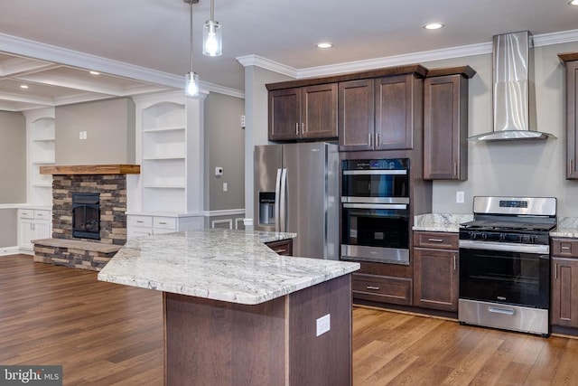 kitchen featuring stainless steel appliances, wall chimney range hood, a stone fireplace, light hardwood / wood-style floors, and a kitchen island