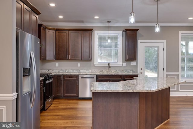 kitchen with light wood-type flooring, stainless steel appliances, light stone counters, and hanging light fixtures