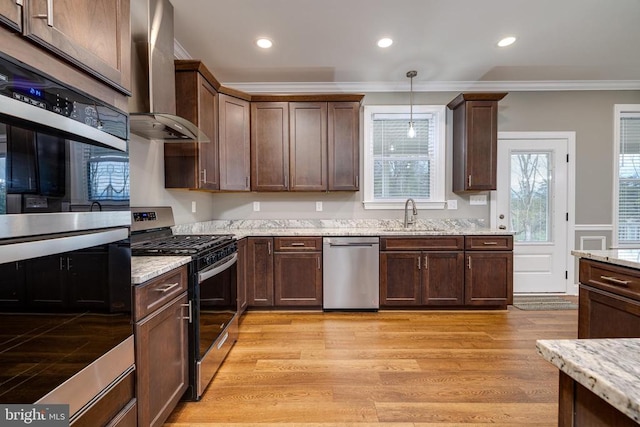 kitchen with light stone countertops, light wood-type flooring, stainless steel appliances, wall chimney range hood, and hanging light fixtures