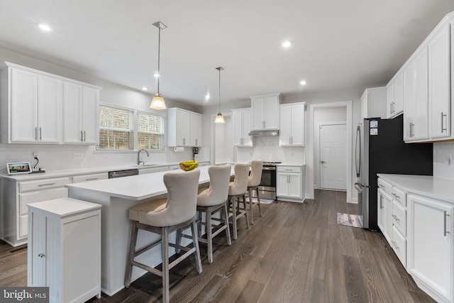 kitchen with white cabinetry, stainless steel appliances, a kitchen breakfast bar, dark hardwood / wood-style flooring, and a kitchen island