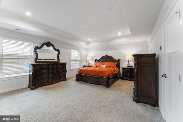 bedroom with a raised ceiling, light carpet, and multiple windows