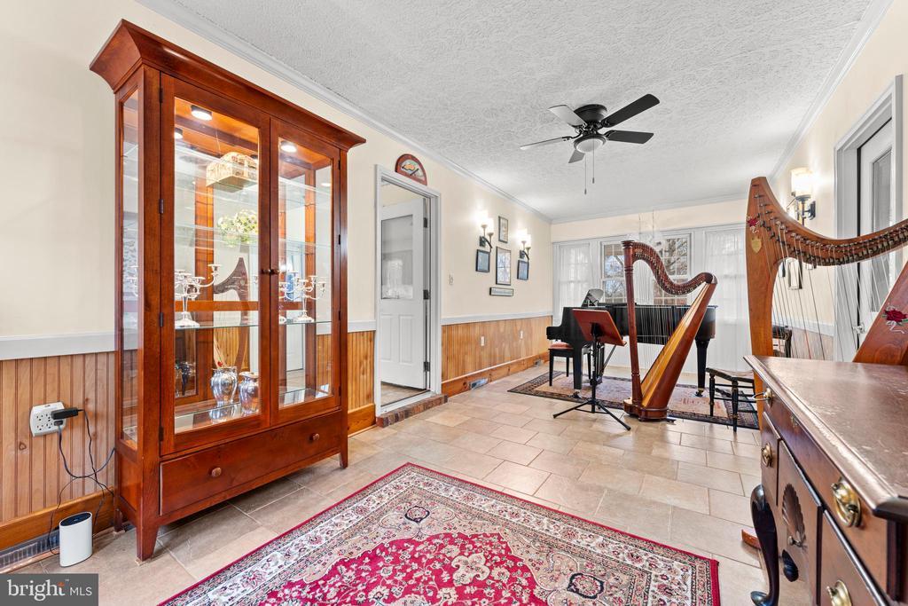 interior space featuring a textured ceiling, ceiling fan, crown molding, wood walls, and light tile patterned flooring