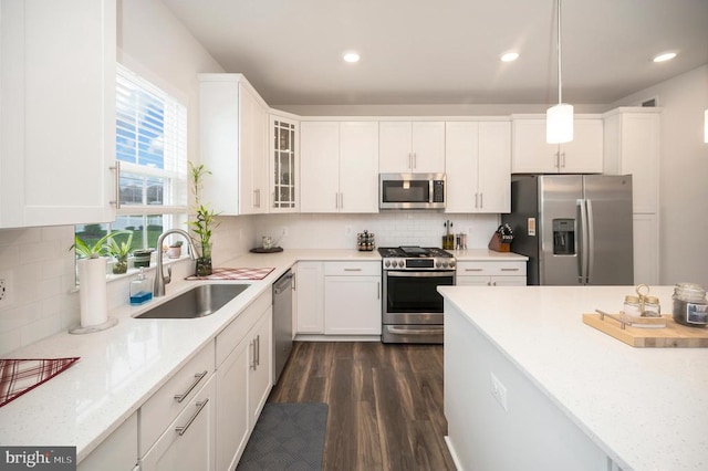 kitchen featuring appliances with stainless steel finishes, dark wood-type flooring, sink, pendant lighting, and white cabinetry