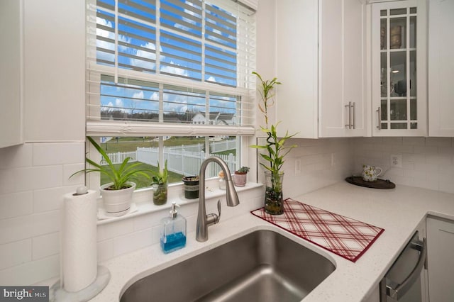 kitchen featuring tasteful backsplash, sink, white cabinets, and stainless steel dishwasher