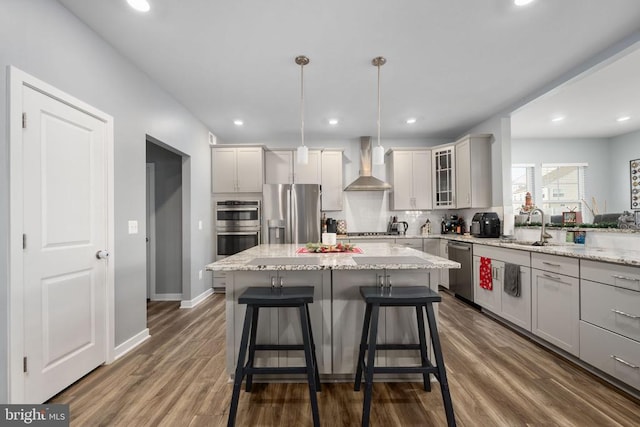 kitchen featuring a center island, dark wood-type flooring, hanging light fixtures, wall chimney range hood, and appliances with stainless steel finishes