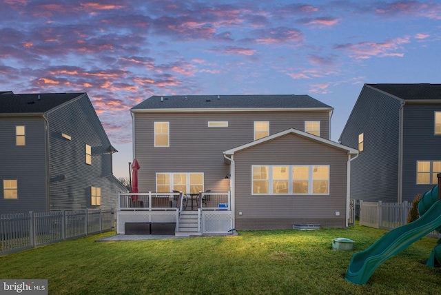 back house at dusk with a deck, a playground, and a yard