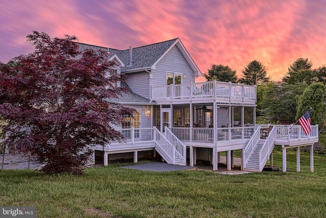 back house at dusk featuring a sunroom, a lawn, and a wooden deck