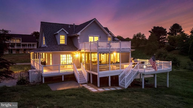 back house at dusk with a lawn, a sunroom, a balcony, and a wooden deck