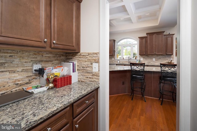 kitchen featuring light stone countertops, backsplash, coffered ceiling, dark wood-type flooring, and beam ceiling