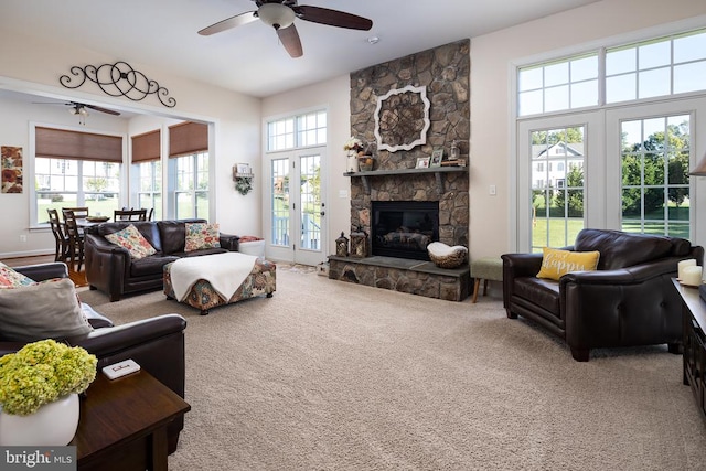 carpeted living room with ceiling fan and a stone fireplace