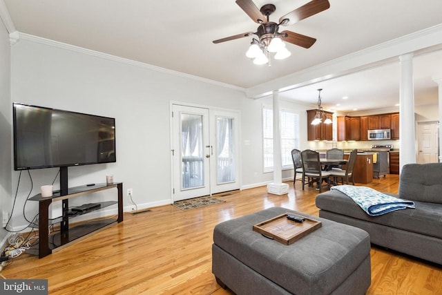 living room with ornate columns, ornamental molding, ceiling fan with notable chandelier, and light hardwood / wood-style flooring