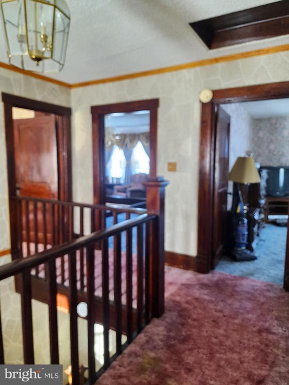 corridor with a textured ceiling, carpet floors, ornamental molding, and a notable chandelier