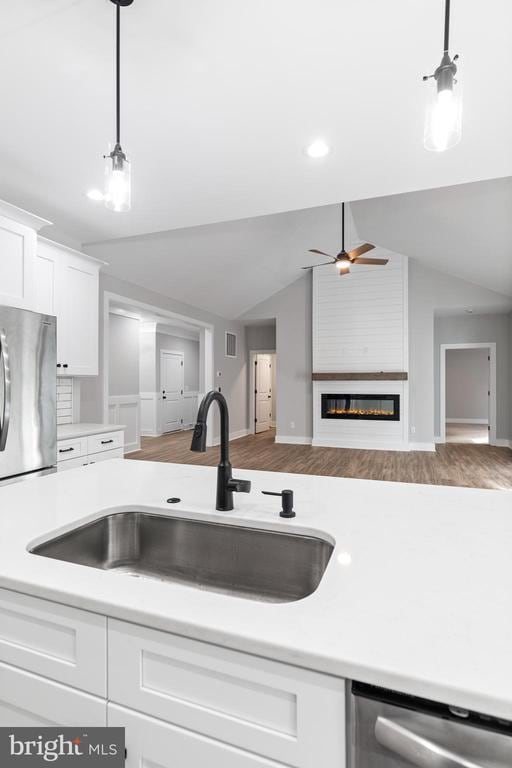 kitchen with lofted ceiling, white cabinets, sink, a fireplace, and stainless steel appliances