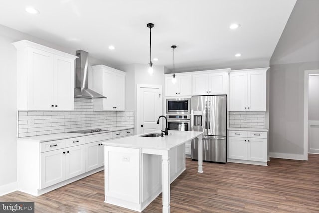 kitchen featuring wall chimney range hood, hanging light fixtures, sink, appliances with stainless steel finishes, and white cabinetry