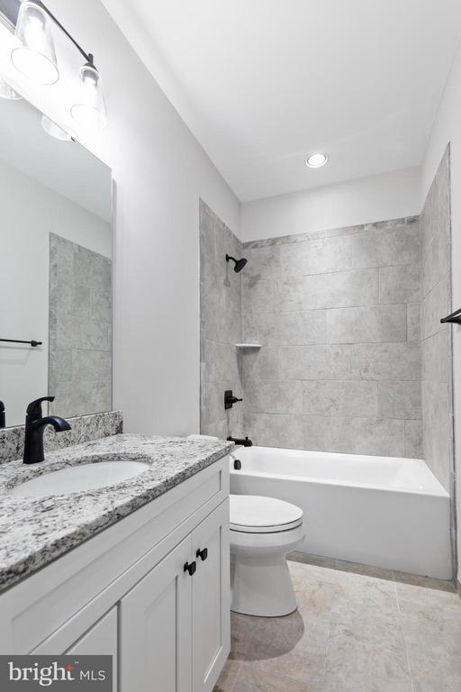 full bathroom with tile patterned flooring, vanity, tiled shower / bath combo, and toilet