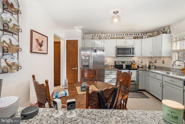 kitchen with sink, backsplash, gray cabinets, light tile patterned flooring, and appliances with stainless steel finishes