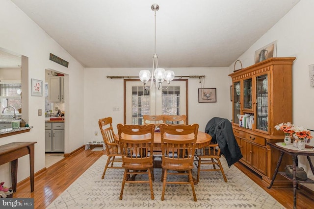 dining space featuring a notable chandelier, light wood-type flooring, lofted ceiling, and sink