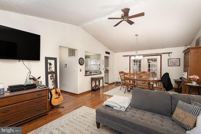 living room with ceiling fan with notable chandelier, light wood-type flooring, and vaulted ceiling