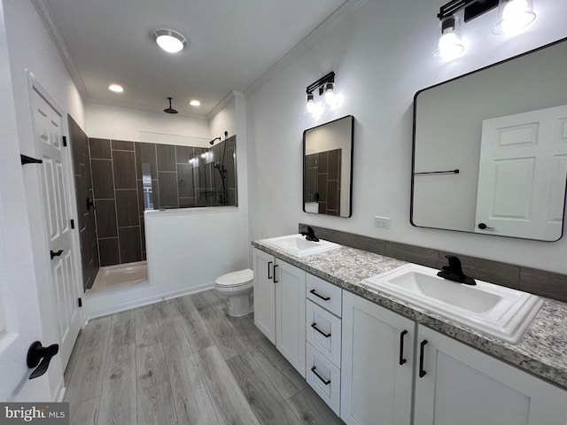 bathroom featuring a tile shower, ornamental molding, toilet, vanity, and hardwood / wood-style flooring