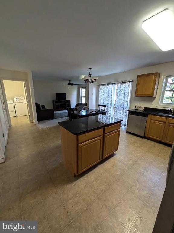 kitchen with ceiling fan with notable chandelier, sink, stainless steel dishwasher, washer and dryer, and a kitchen island