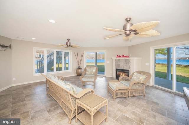 living room with a tiled fireplace, ceiling fan, and a water view