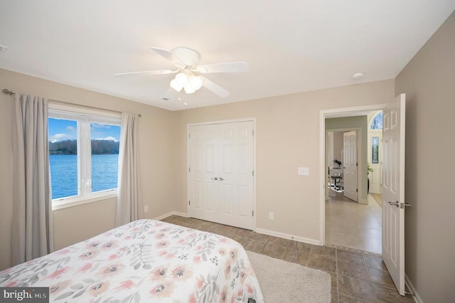 bedroom with ceiling fan, a water view, and a closet