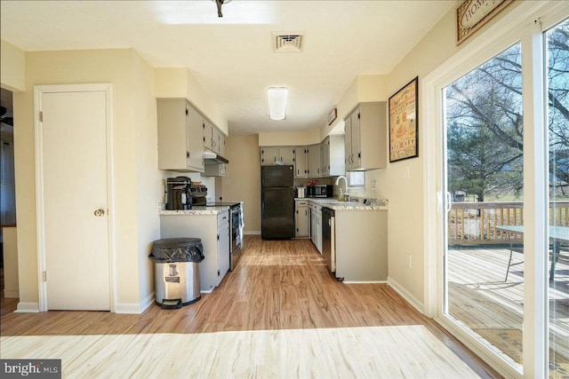 kitchen with appliances with stainless steel finishes, light wood-type flooring, light stone counters, and gray cabinetry