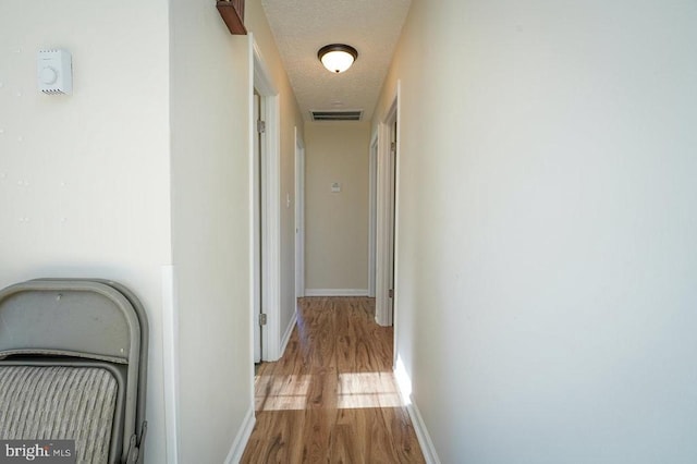 hallway with light hardwood / wood-style flooring and a textured ceiling