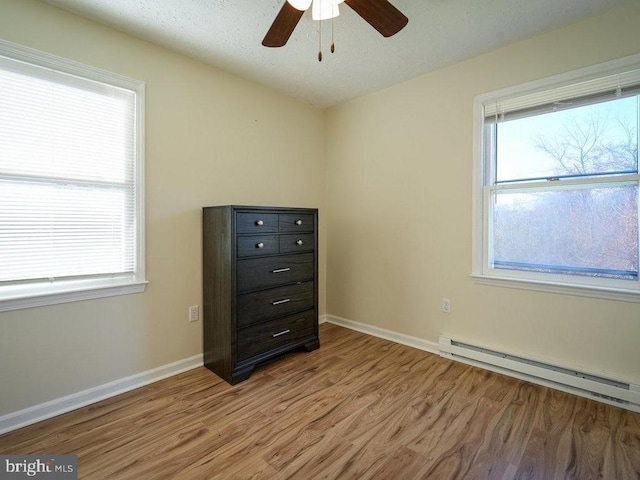 unfurnished bedroom with ceiling fan, multiple windows, a baseboard radiator, and light hardwood / wood-style flooring