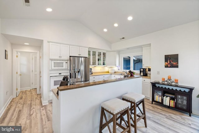 kitchen with white appliances, white cabinets, light wood-type flooring, a kitchen bar, and kitchen peninsula