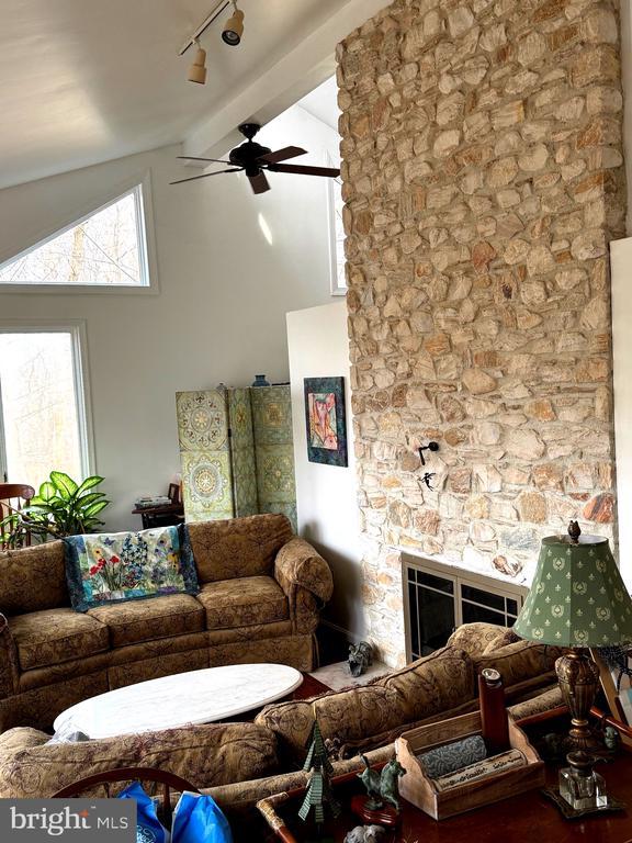 living room with lofted ceiling with beams, ceiling fan, a stone fireplace, and rail lighting