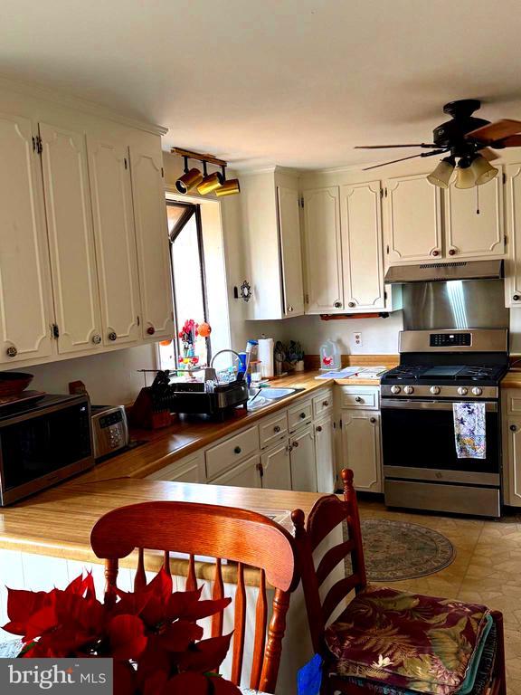 kitchen with white cabinets, ceiling fan, gas stove, and kitchen peninsula