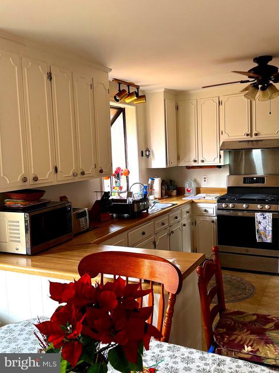 kitchen with white cabinets, gas range, kitchen peninsula, and ceiling fan