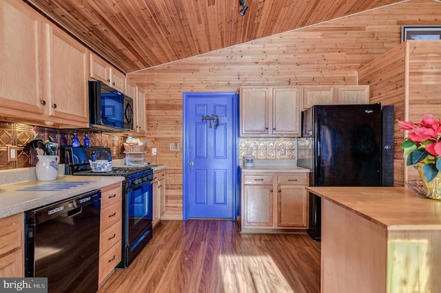 kitchen featuring wooden walls, light brown cabinets, black appliances, and vaulted ceiling