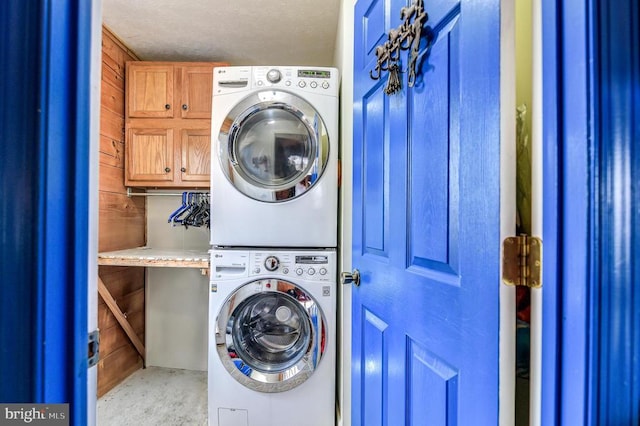 washroom with cabinets, wooden walls, stacked washing maching and dryer, and a textured ceiling