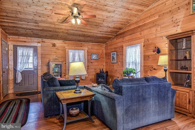 living room with lofted ceiling, a wood stove, wooden walls, ceiling fan, and wood-type flooring