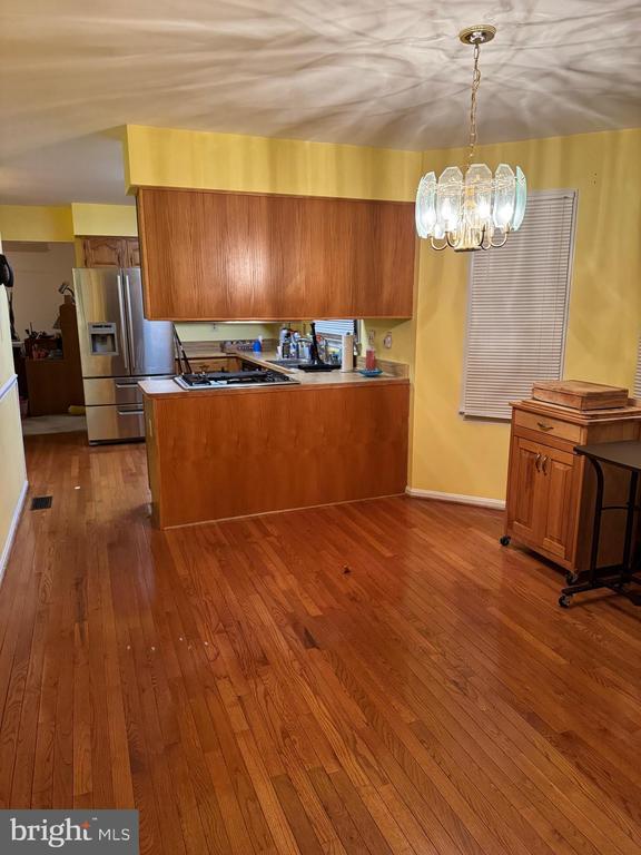 kitchen featuring kitchen peninsula, stainless steel appliances, dark wood-type flooring, pendant lighting, and a notable chandelier