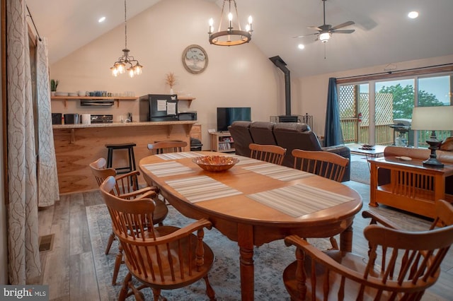 dining space featuring ceiling fan with notable chandelier, wood-type flooring, vaulted ceiling, and a wood stove