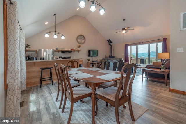 dining area featuring ceiling fan, light hardwood / wood-style floors, a wood stove, and high vaulted ceiling