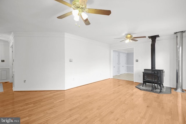 unfurnished living room with ceiling fan, light hardwood / wood-style floors, a wood stove, and crown molding