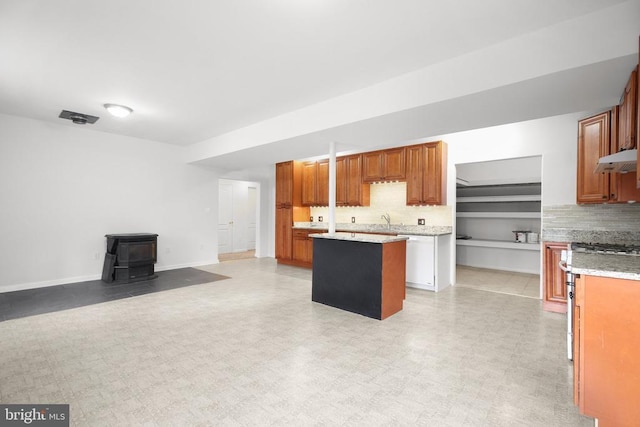 kitchen with decorative backsplash, a center island, a wood stove, and stainless steel stove