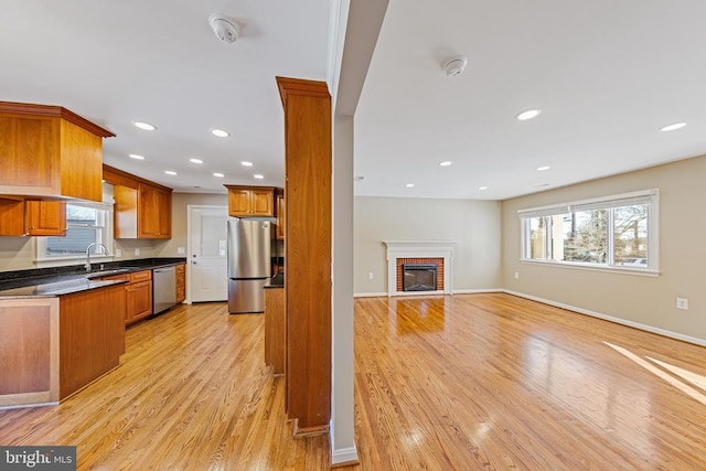 kitchen with light hardwood / wood-style floors, sink, stainless steel appliances, and a brick fireplace