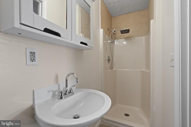 bathroom with a textured ceiling, walk in shower, and sink