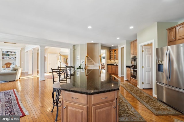 kitchen featuring a center island, decorative columns, dark stone countertops, appliances with stainless steel finishes, and light wood-type flooring