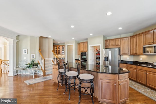 kitchen featuring a center island, dark stone countertops, wood-type flooring, stainless steel appliances, and decorative columns