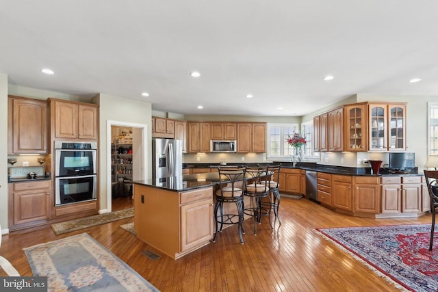 kitchen featuring a center island, dark stone countertops, appliances with stainless steel finishes, light hardwood / wood-style floors, and a kitchen bar