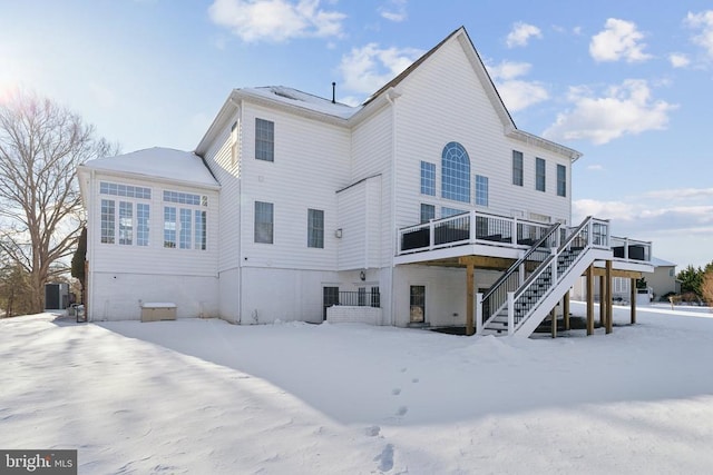 snow covered back of property with central air condition unit and a wooden deck