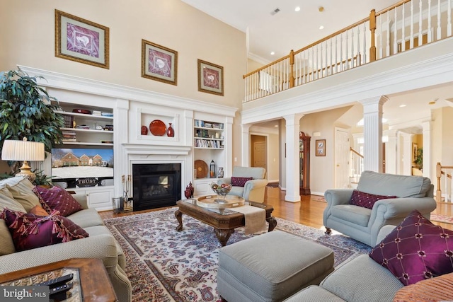 living room featuring wood-type flooring, built in features, a towering ceiling, and decorative columns